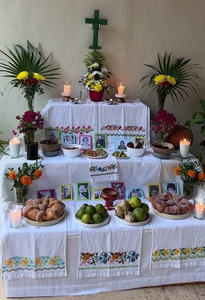 Traditional Janal Pixán altar in Yucatán with photographs, candles, flowers, food, fruit, and a cross.